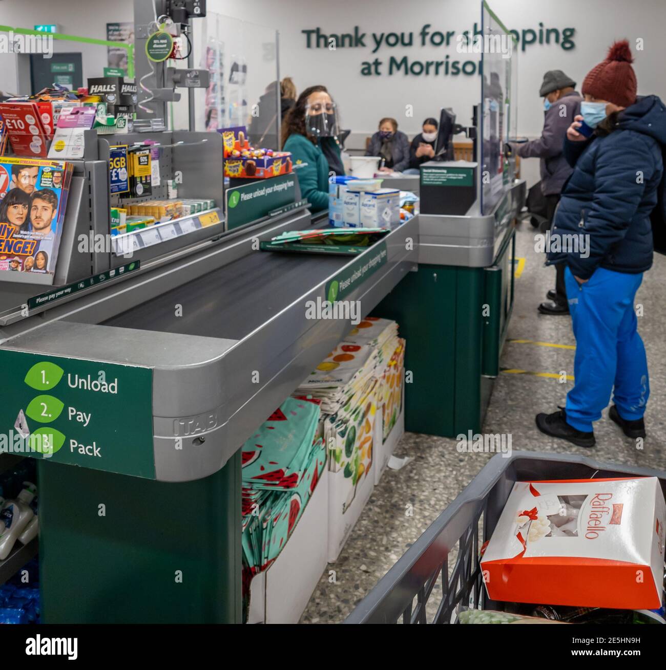 Personale e clienti che indossano la copertura facciale e separati da uno schermo in un supermercato checkout come richiesto dalle norme di sicurezza Covid-19. Foto Stock