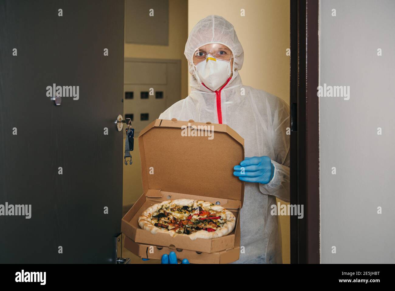 Uomo impiegato in guanti medici e maschera protettiva che consegna la pizza a casa durante l'epidemia di virus. Conservare il servizio alimentare in quarantena coronavirus Foto Stock