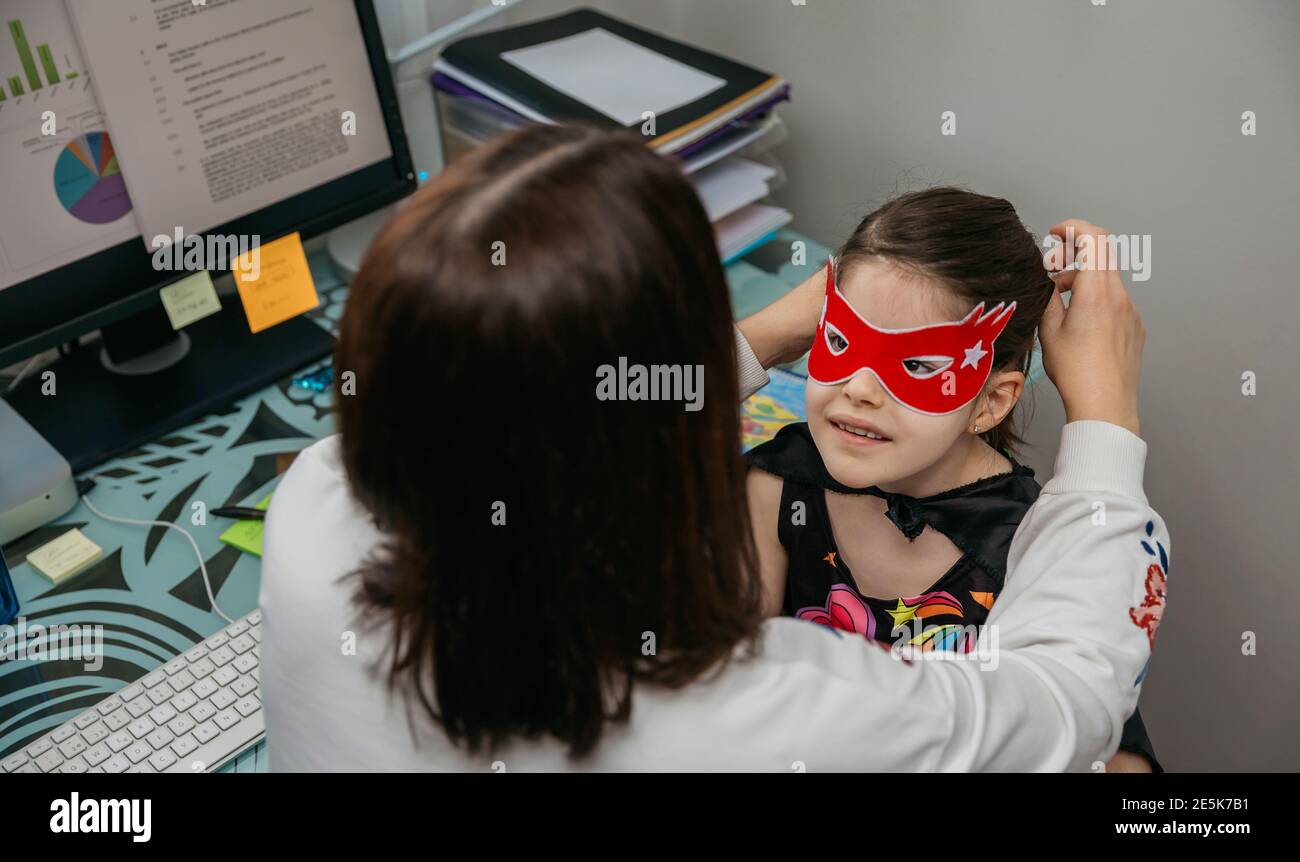 Donna telelavoro e mettere maschera costume su sua figlia Foto Stock