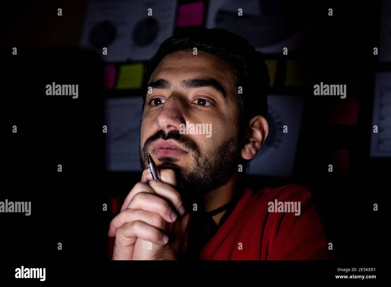 Il giovane sta pensando davanti al suo laptop a. le ore di straordinario nel suo ufficio buio Foto Stock