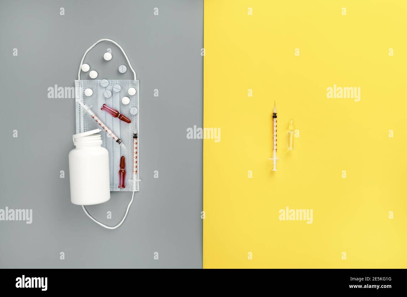 Flacone mock-up con pillole, siringhe, fiale e maschera medica su sfondo giallo e grigio alla moda. Medicina di base. Vaccino del coronavirus Foto Stock