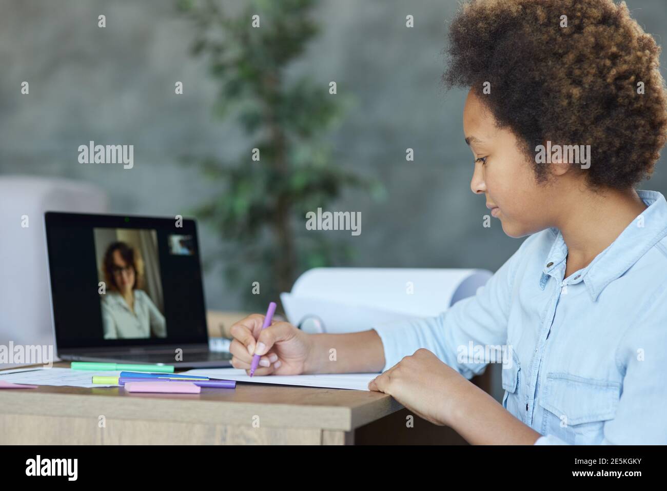 Messa a fuoco mista razza scolara disegno su carta con marcatori colorati, utilizzando il laptop durante la video lezione online con l'insegnante a casa Foto Stock