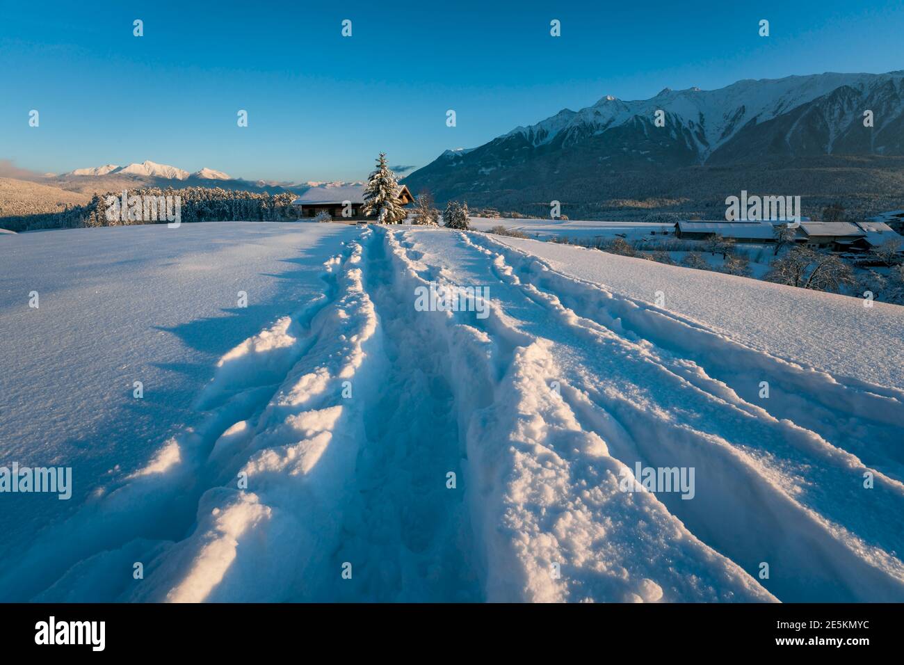 Sentiero innevato nel paesaggio invernale soleggiato in montagna verso la tipica casa austriaca durante il tramonto a Wildermieming, Tirol, Austria Foto Stock