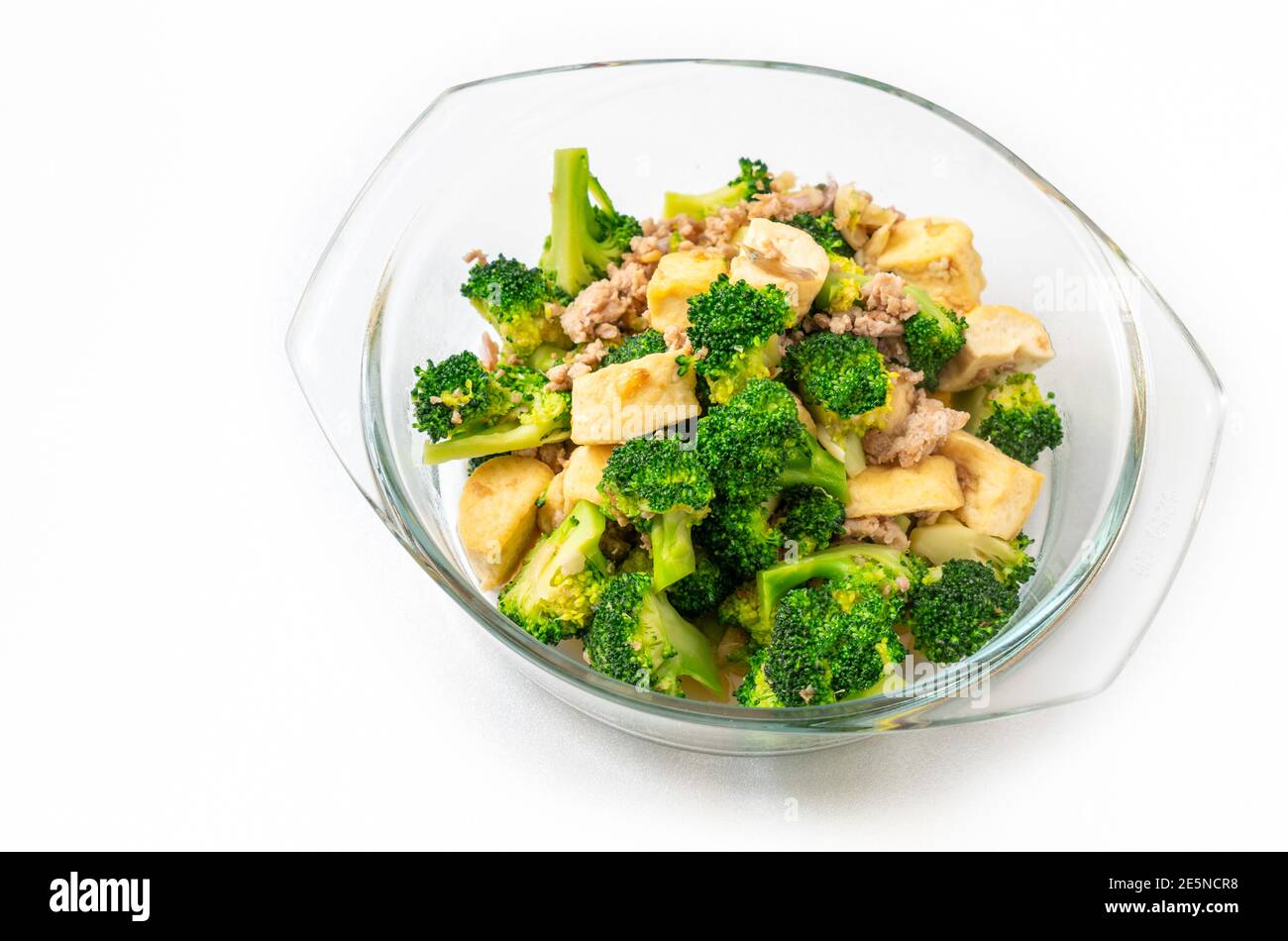 Cibo tailandese fatto in casa, broccoli fritti in padella con tofu e maiale macinato, cibo in una ciotola di vetro trasparente su sfondo bianco. Foto Stock