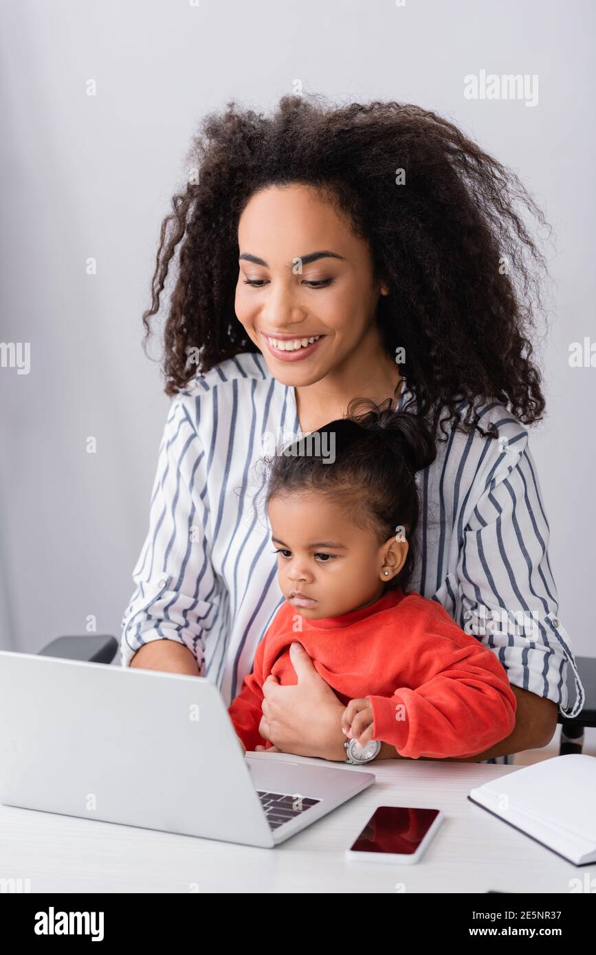 felice freelance afroamericano seduto con la figlia del toddler mentre lavora da casa Foto Stock
