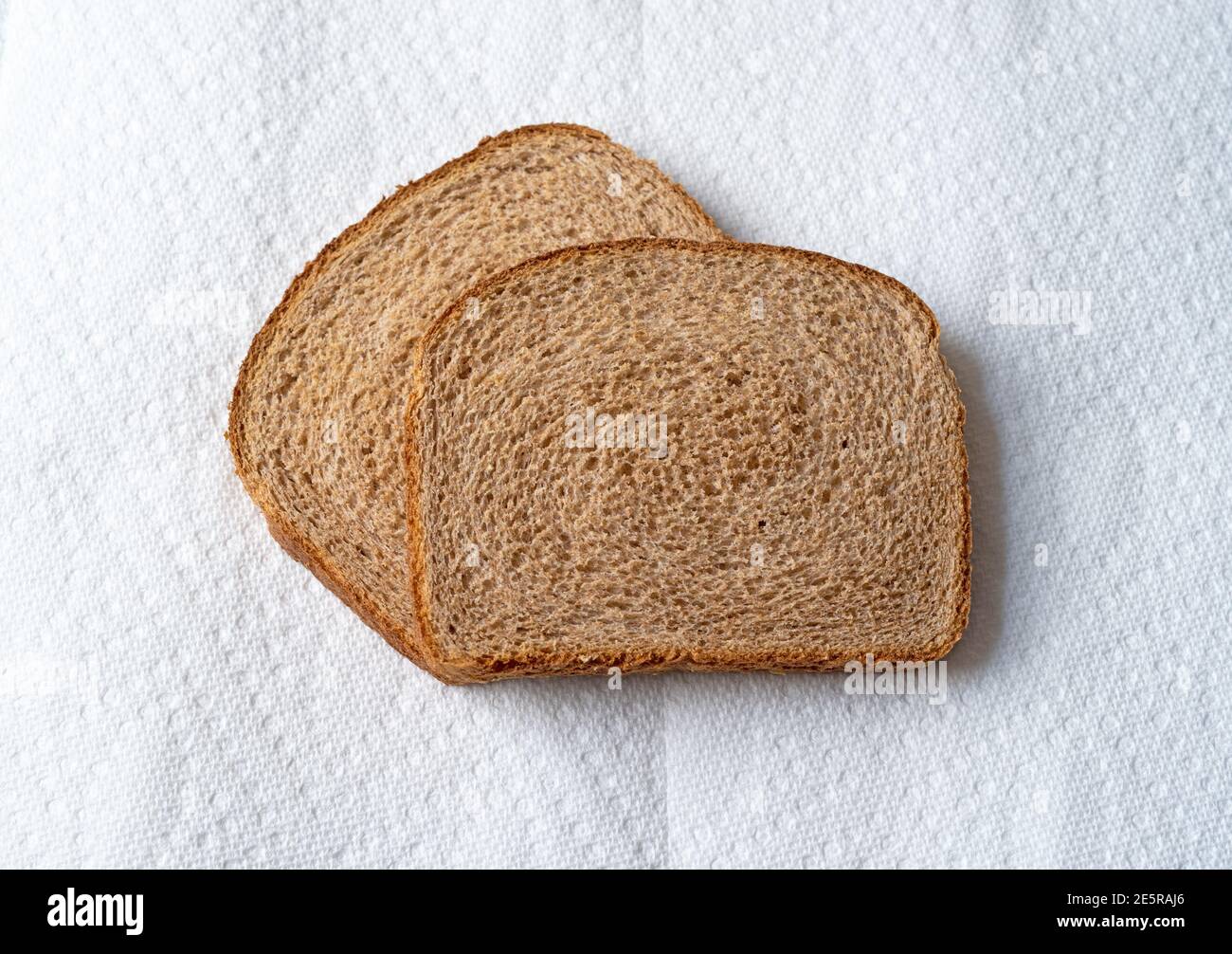 Vista dall'alto di due fette di pane di grano su asciugamani di carta bianca con luce naturale. Foto Stock