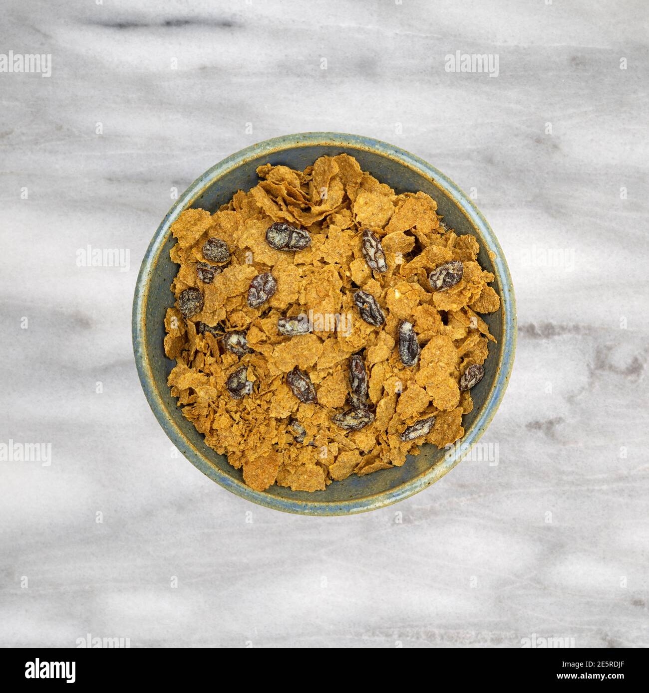Vista dall'alto di una ciotola piena di fiocchi di crusca e uvetta per la colazione, cereali su sfondo di marmo grigio. Foto Stock