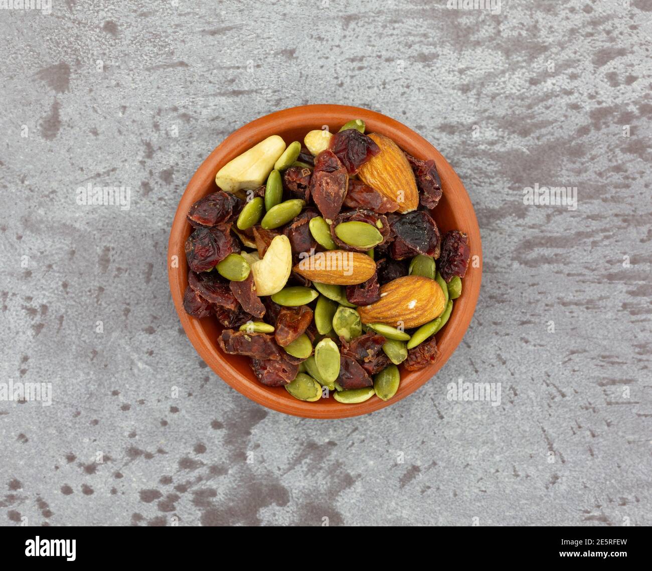 Vista dall'alto di una piccola ciotola piena di semi, noci e frutta su sfondo grigio. Foto Stock