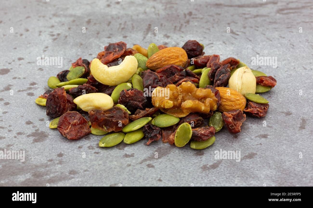 Vista laterale di una piccola porzione di semi, noci e frutta su sfondo grigio. Foto Stock