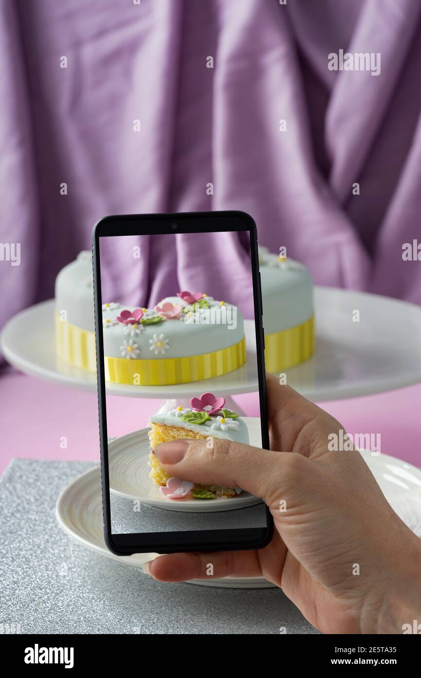 Donna che fa foto della torta di celebrazione decorata fondente con lei telefono su sfondo viola Foto Stock