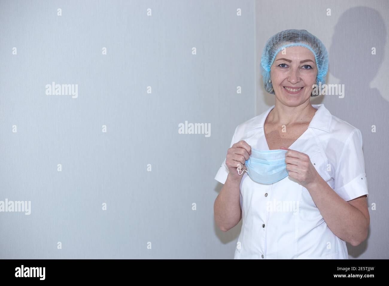 Vaccinazione contro il coronavirus. L'infermiere sorride, tenendo una maschera medica, su uno sfondo chiaro, copiare lo spazio a sinistra. Preparazione per il processo Foto Stock