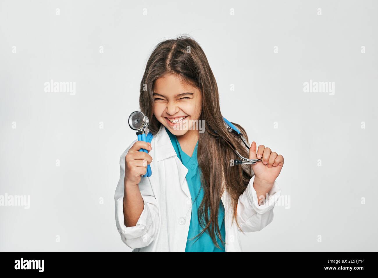 Ritratto di razza mista bambina vestita da medico con stetoscopio in mano, lei posa, sorridendo e guardando la macchina fotografica. Isolato su bianco Foto Stock