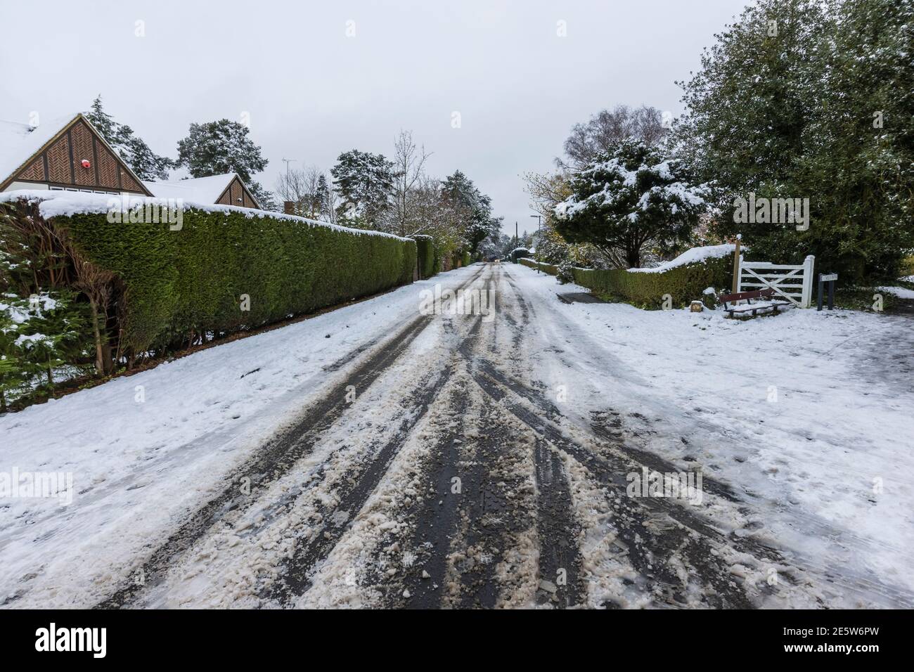 Auto e pneumatici di veicoli cingono in su neve churned girando per schiaffo in Hollybank Road, una strada suburbana in Hook Heath, Woking dopo una nevicata in inverno Foto Stock