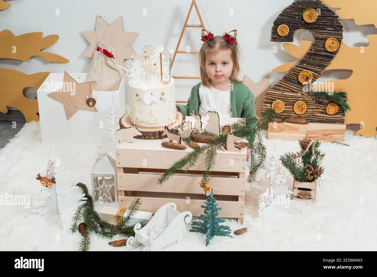 Decorazioni per compleanno invernali per bambini. 2 anni. Carino bambina in  un cardigan verde vicino torta di compleanno bianca Foto stock - Alamy