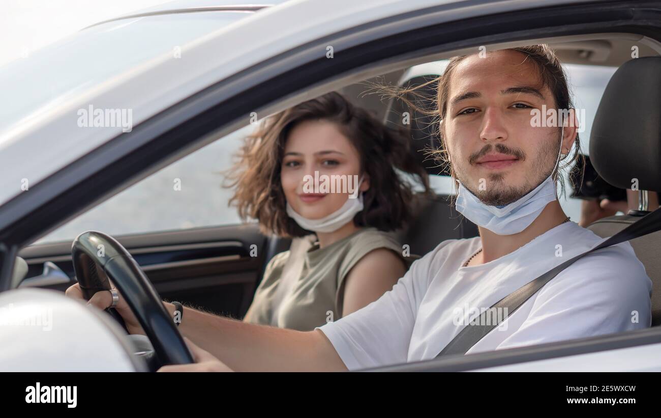 I giovani che indossano una maschera protettiva per il viso sono seduti sui sedili anteriori del passeggero e guardano la telecamera. Virus corona pandemic Concept.viaggio su strada Foto Stock