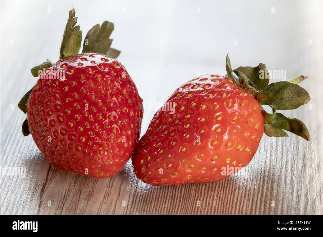 Intere due fragole con foglia su fondo di legno. Fragole fresche mature isolate. Concetto di alimentazione sana. Messa a fuoco impilata. Foto Stock