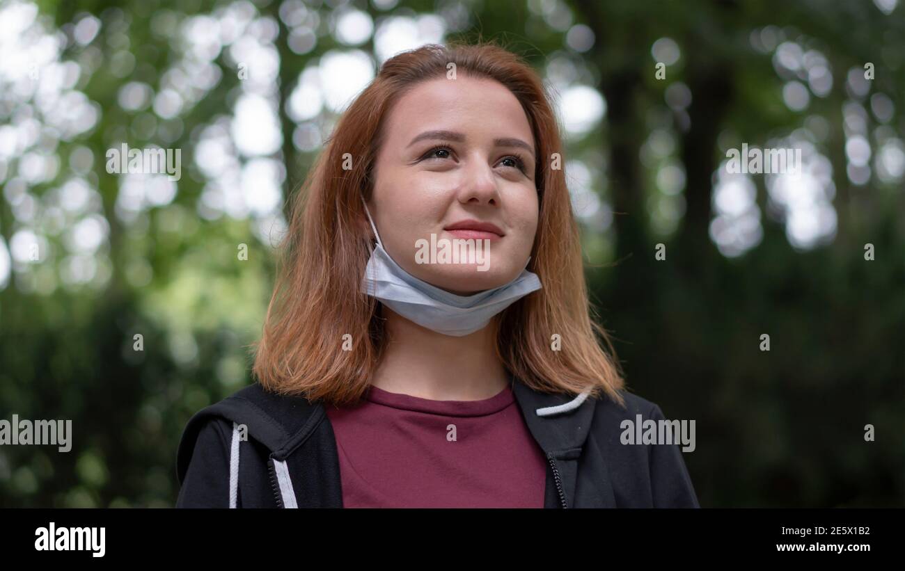 Giovane donna beatiful che guarda lontano mentre la sua maschera sotto il suo volto nella foresta in mezzo covid-19 pandemic. Foto Stock