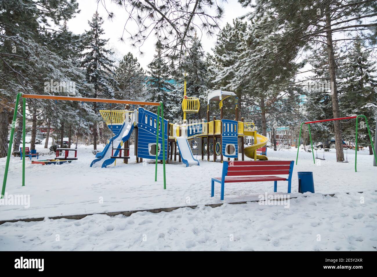 In inverno, il colorato parco giochi è coperto di neve. In primo piano è una panca. Foto Stock