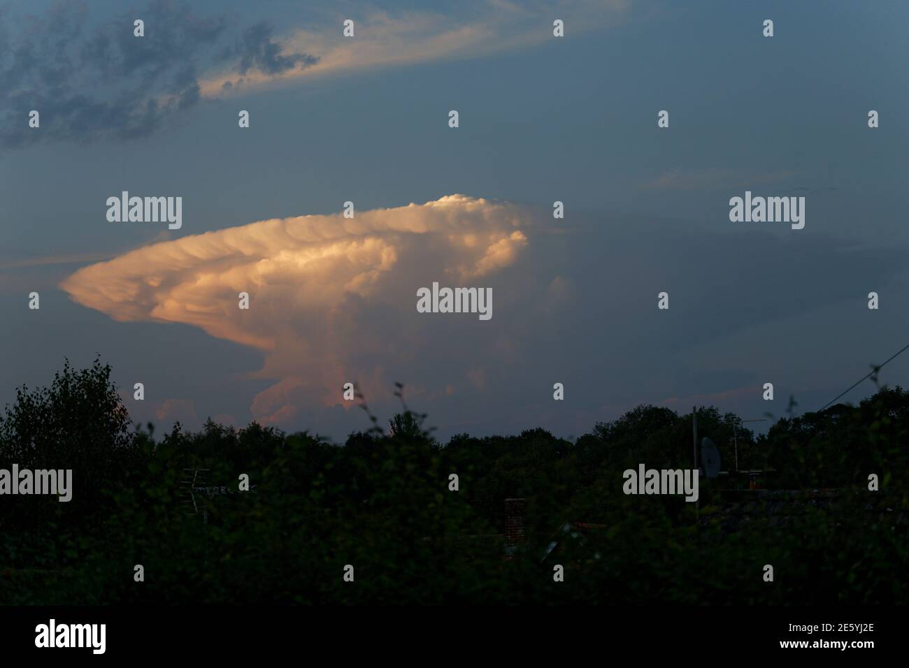 Nube tuono distante nella classica forma incudine illuminata da un sole di sera basso Foto Stock