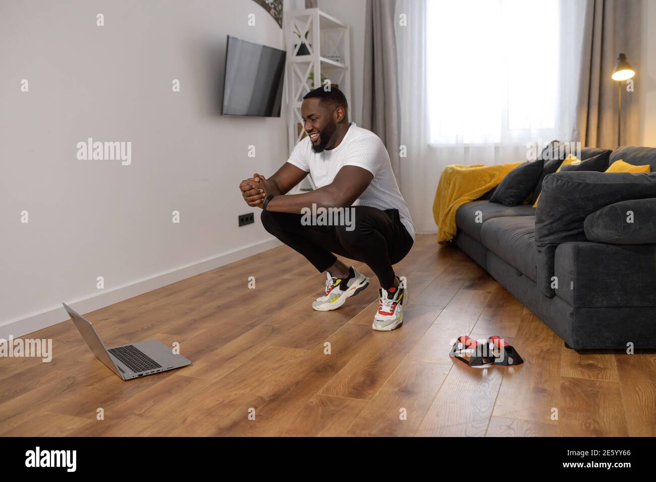 Bel giovane afroamericano sta tenendo il suo corpo in posizione squat, diventando attivo mentre isolato, imparare dal corso di yoga online, fitness Foto Stock