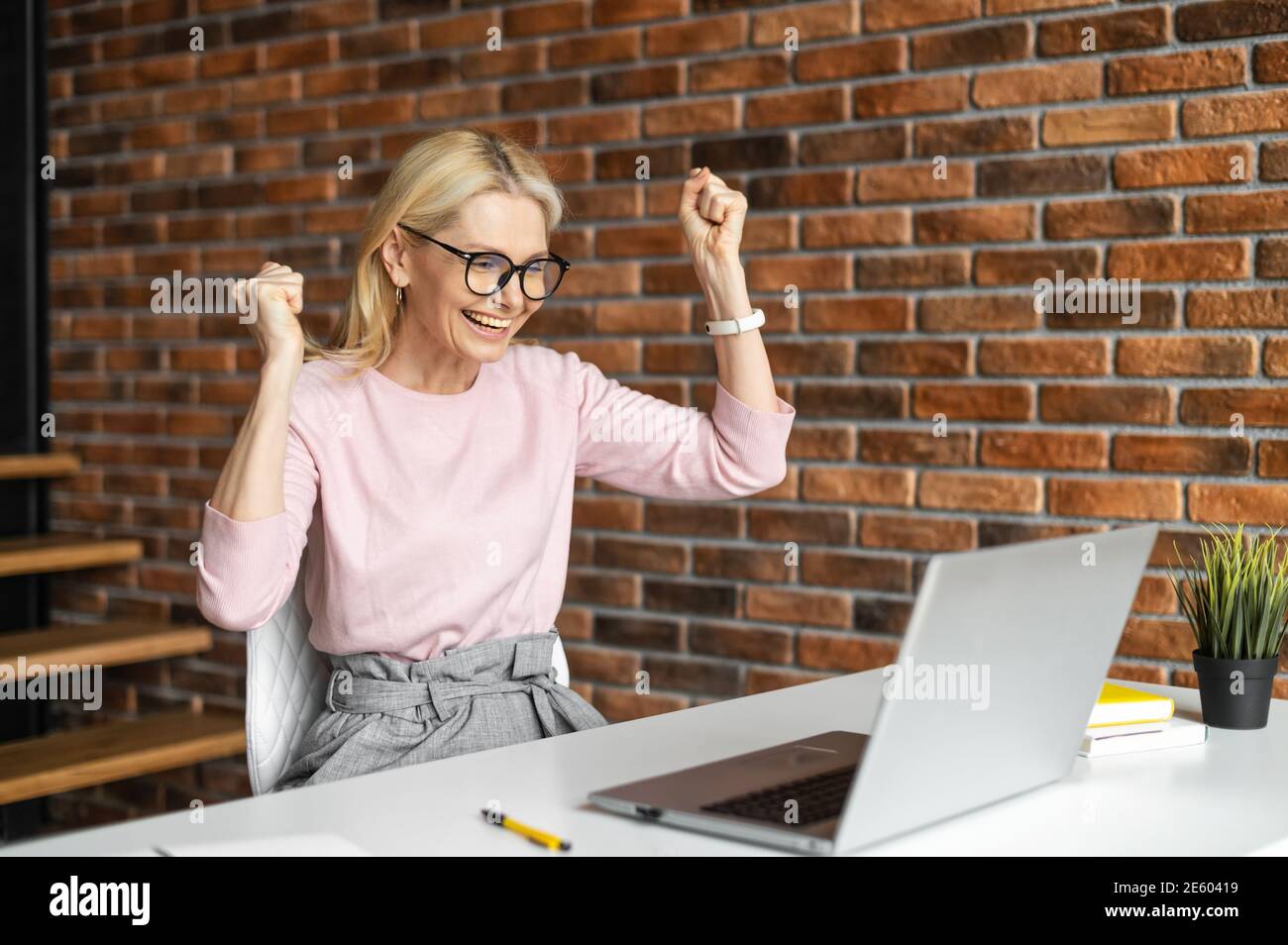 Una donna d'affari molto gioiosa guarda lo schermo del laptop e alzando le braccia come segno di vittoria, una donna felice ride con trionfo, vincendo nel gioco, avendo Foto Stock