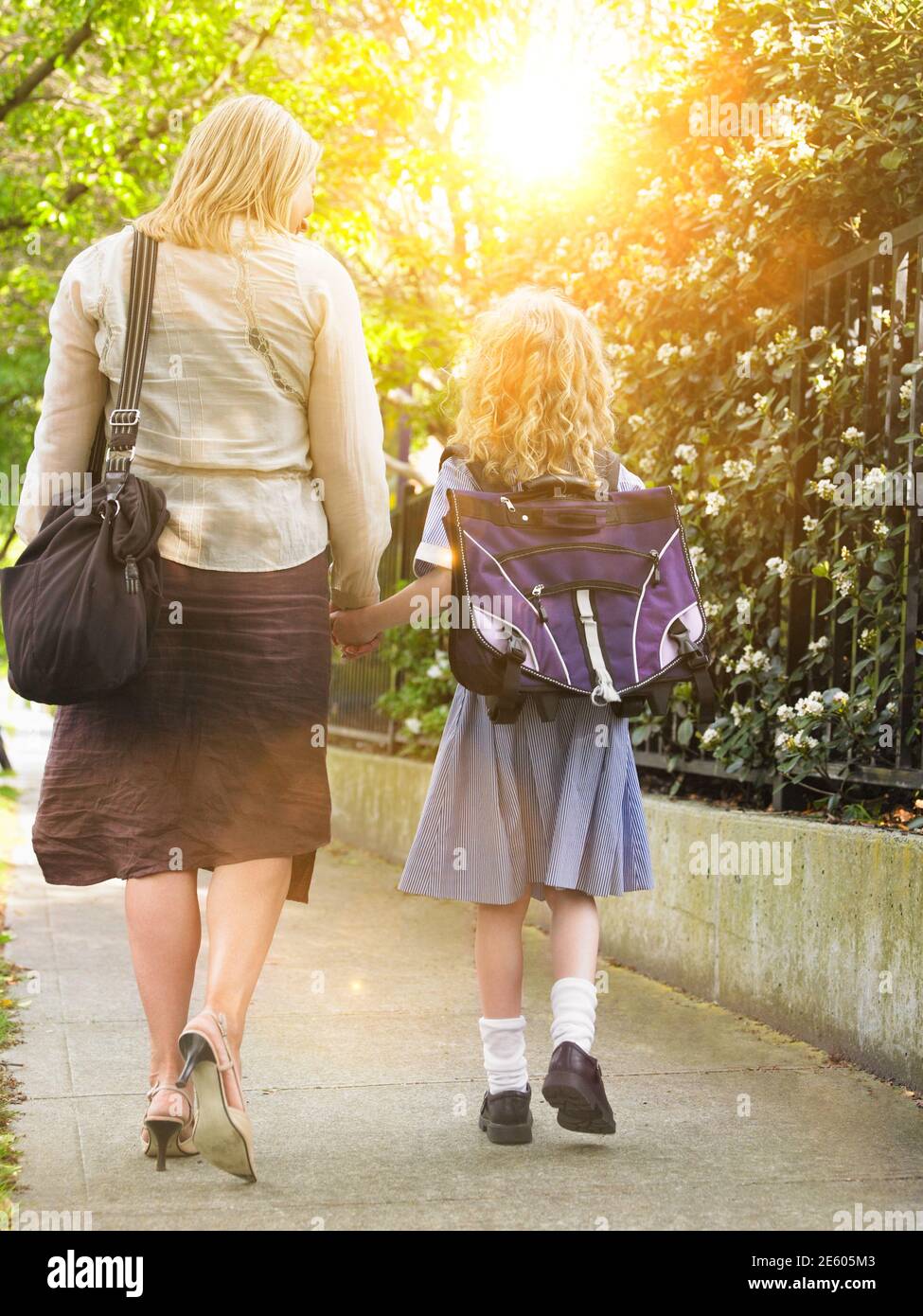 Vista posteriore della studentessa che cammina con la madre sul marciapiede Foto Stock
