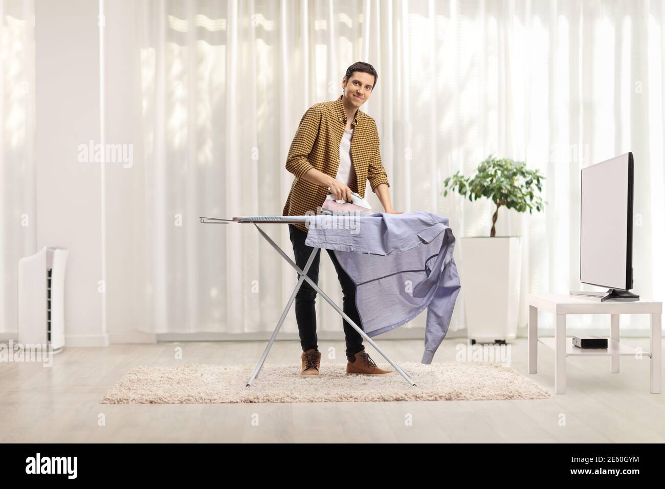 Giovane che stira una camicia a casa in un soggiorno camera Foto Stock