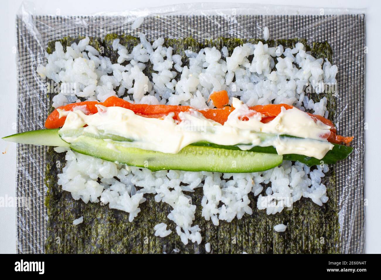 su una foglia di nori si trova riso, cetriolo, pesce e formaggio morbido, facendo sushi Foto Stock