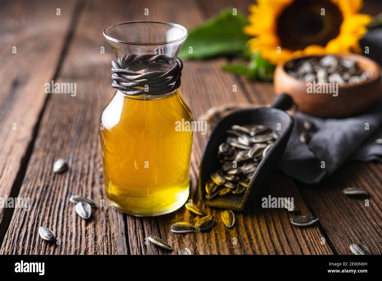 Olio di girasole in un vaso di vetro, decorato con semi interi e fiori su un tavolo di legno Foto Stock