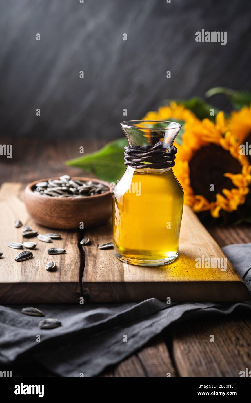 Olio di girasole in un vaso di vetro, decorato con semi interi e fiori su un tavolo di legno Foto Stock