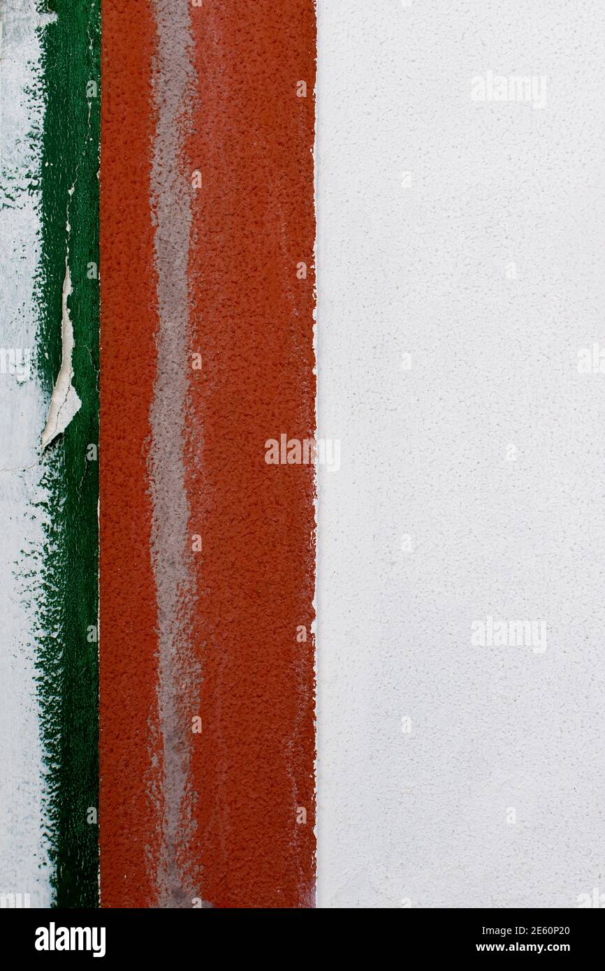 Dettaglio di una vecchia parete di cemento bianca con bordo di due strisce verticali graffiate in vernice verde e rossa sul lato sinistro del telaio. Disegno astratto Foto Stock