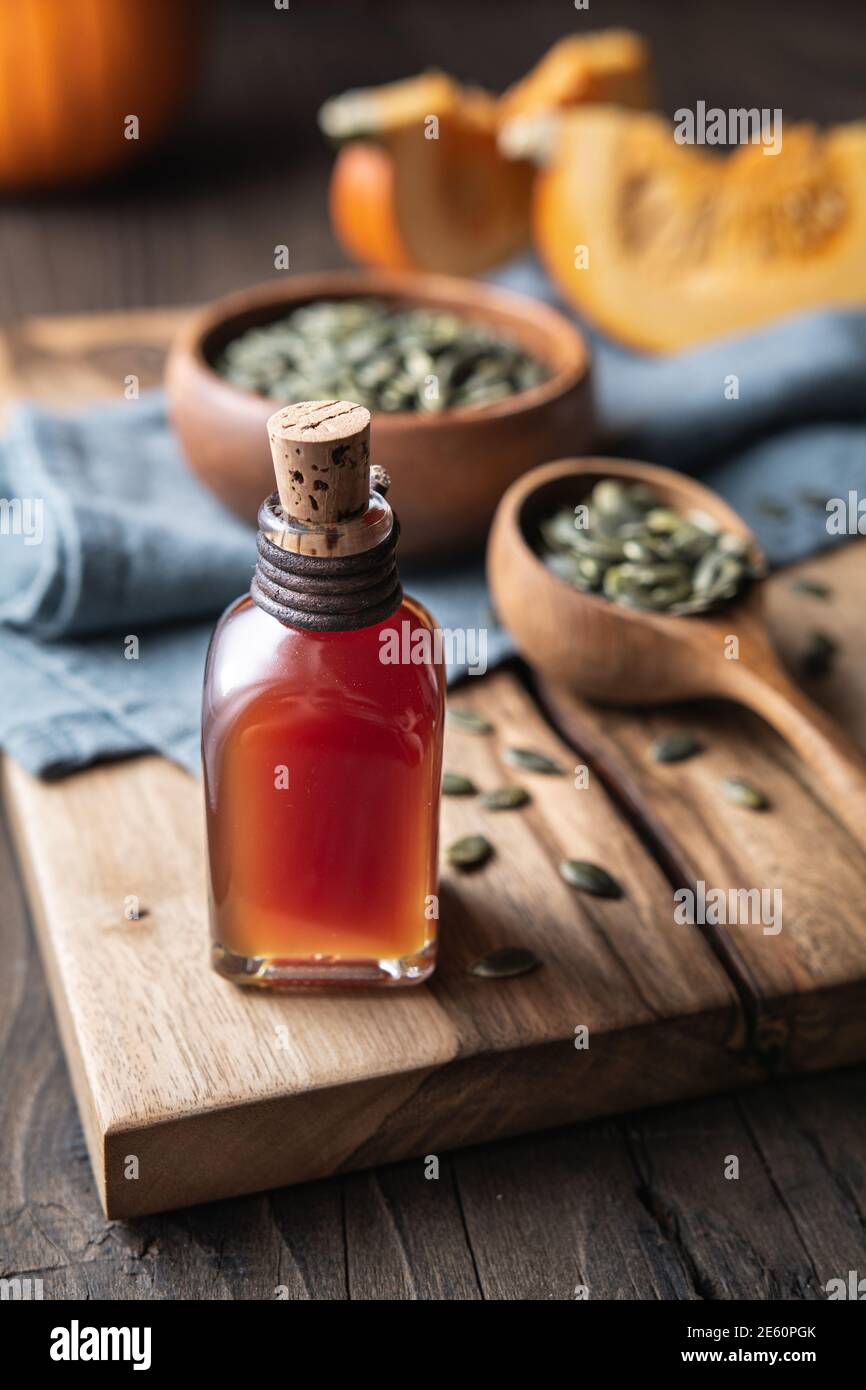 Olio di semi di zucca pressato a freddo in una bottiglia di vetro, decorato con semi sbucciati su un tavolo di legno Foto Stock