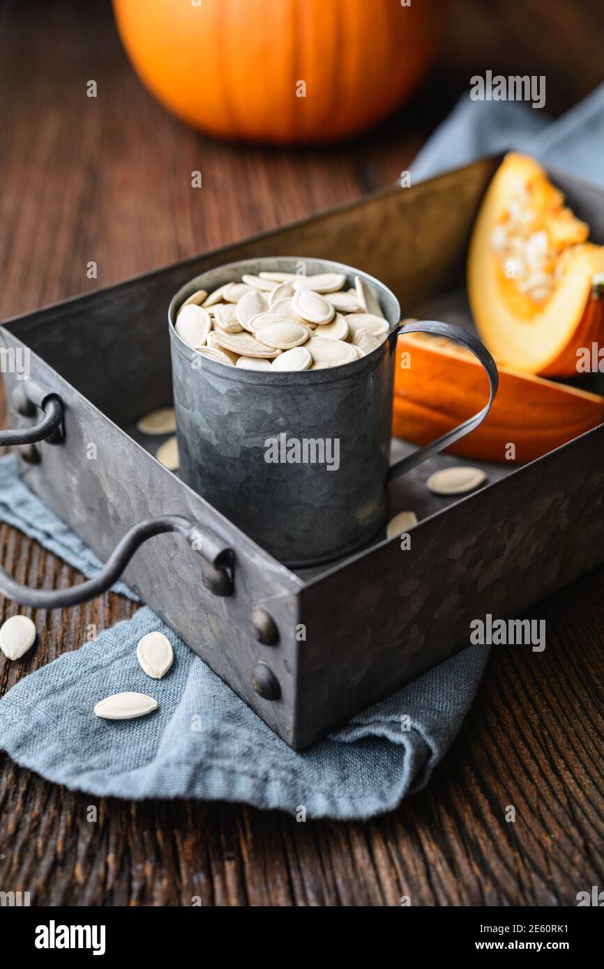 Semi di zucca sgusciati in tazza metallica, decorati con fette di zucca su tavolo di legno Foto Stock