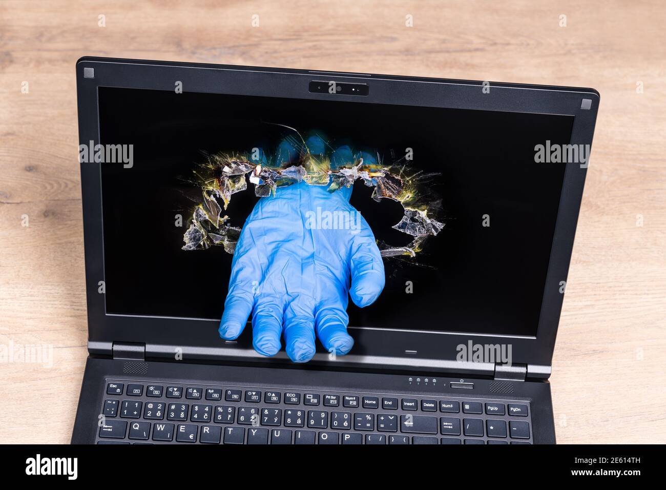 Dettagli del notebook con immaginario aiuto mano in guanto blu che si stacca dal foro perforato nel display. Concetto di assistenza sanitaria a distanza nella malattia di coronavirus. Foto Stock