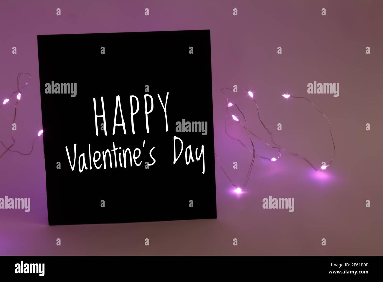 Buon giorno di San Valentino testo sulla carta nera. Luci rosa sullo sfondo. Febbraio 14 concetto di San Valentino. Foto Stock