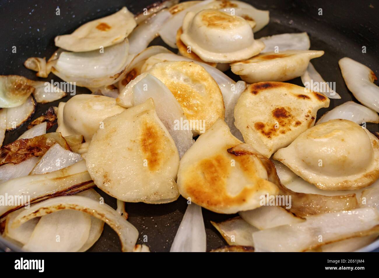 Primo piano di pierogi e cipolle cucinate su una padella di frittura a stovetop. Foto Stock