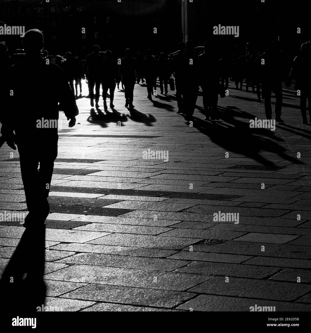 Ombre di persone che camminano al tramonto sul pavimento in pietra della città pre-pandemica di Milano, Lombardia, Italia Foto Stock