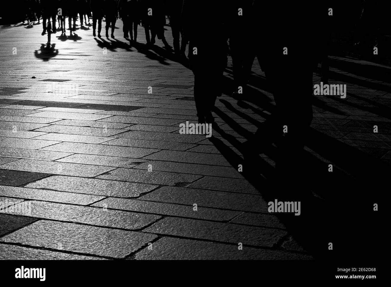 Ombre di persone che camminano al tramonto sul pavimento in pietra della città pre-pandemica di Milano, Lombardia, Italia Foto Stock
