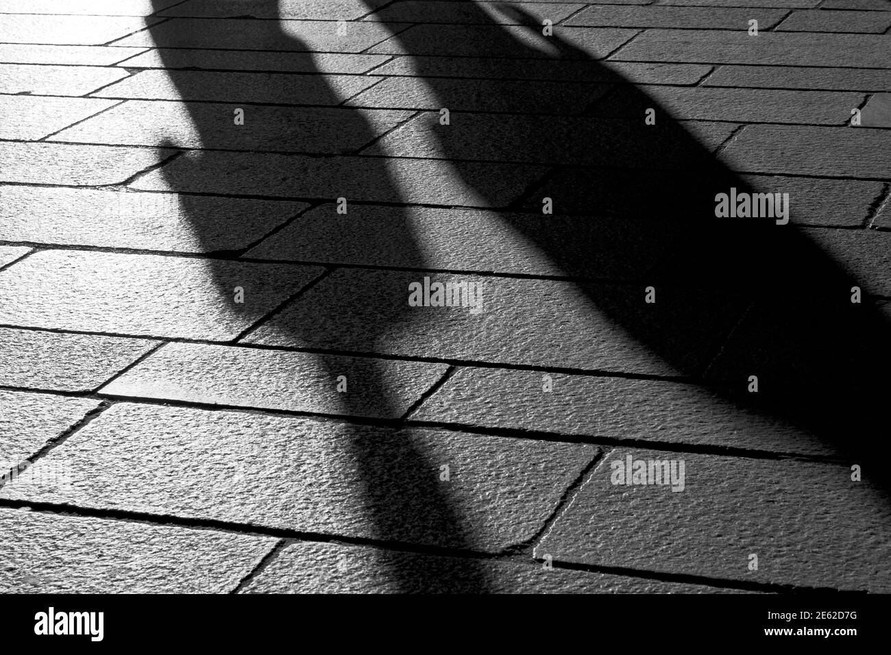 Ombre di persone che camminano al tramonto sul pavimento in pietra della città pre-pandemica di Milano, Lombardia, Italia Foto Stock