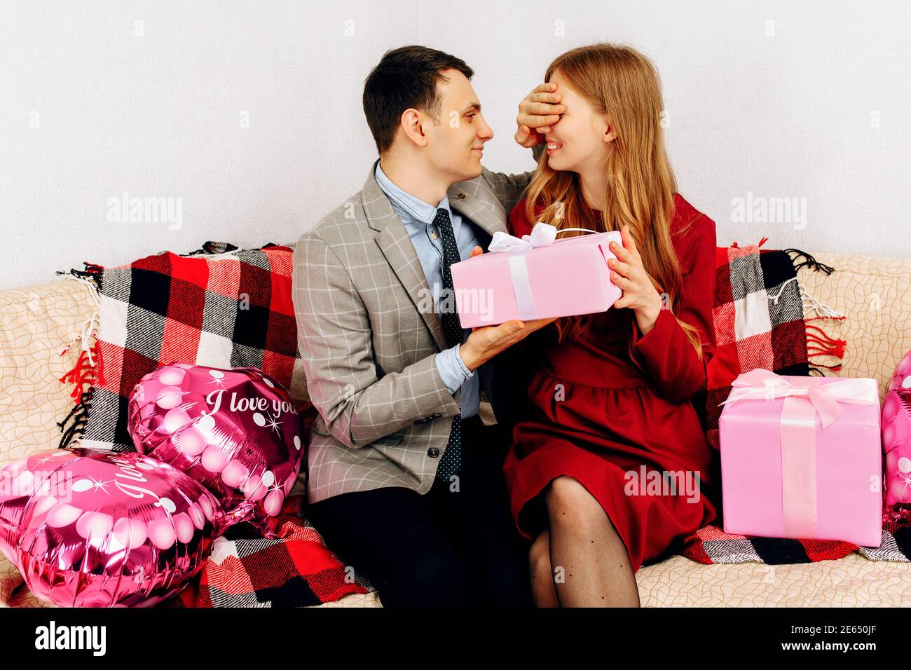 Data romantica. Uomo elegante che copre gli occhi alla donna dando dono di San Valentino a casa Foto Stock