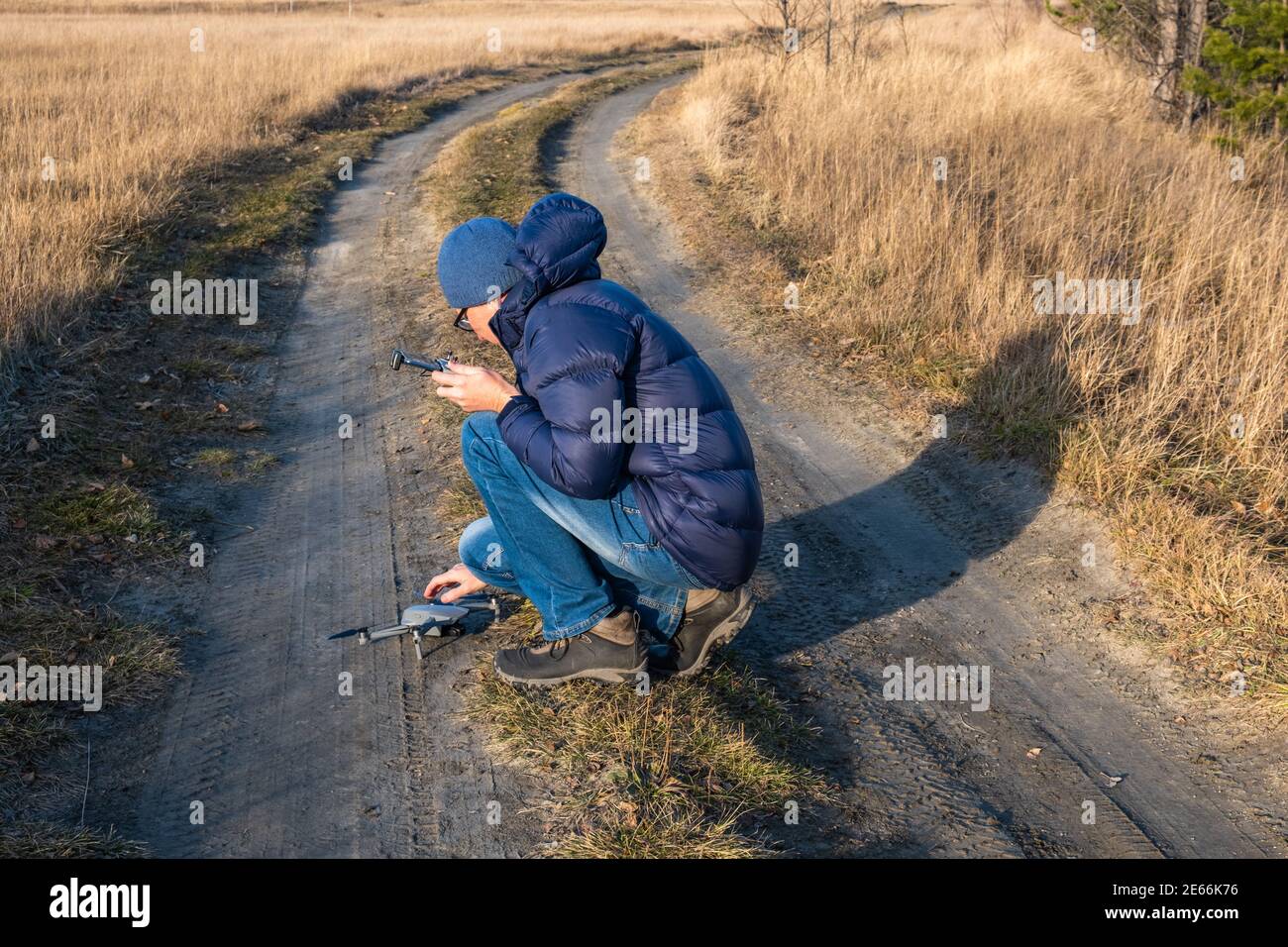 Un uomo turistico con un telecomando, installa un drone su una strada sterrata in un campo in una giornata di sole chiaro per scattare foto e video della natura autunnale. Foto Stock