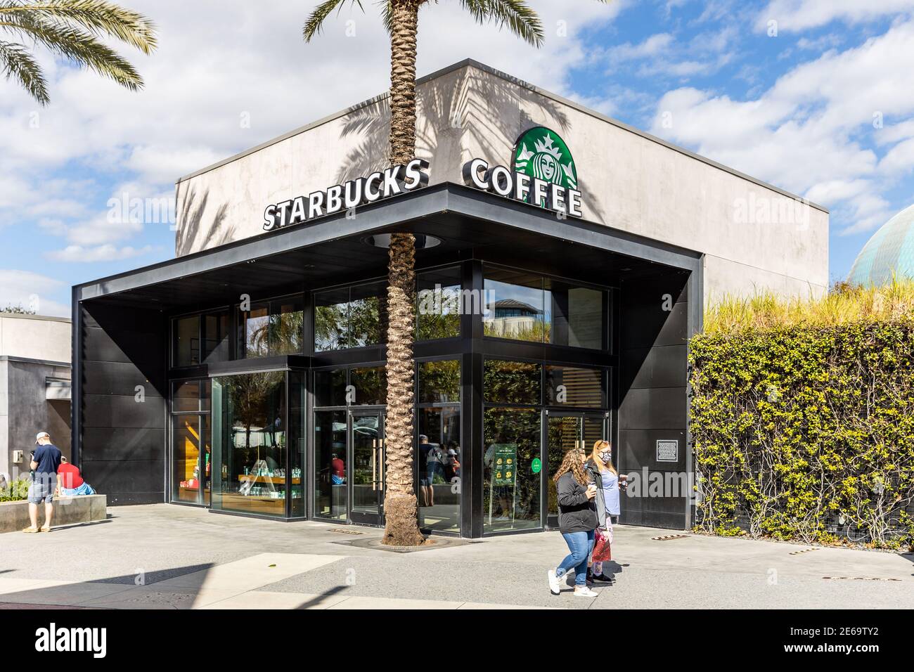 Un moderno edificio Starbucks Coffee con una palma che cresce la loro facciata e la gente che cammina. Foto Stock