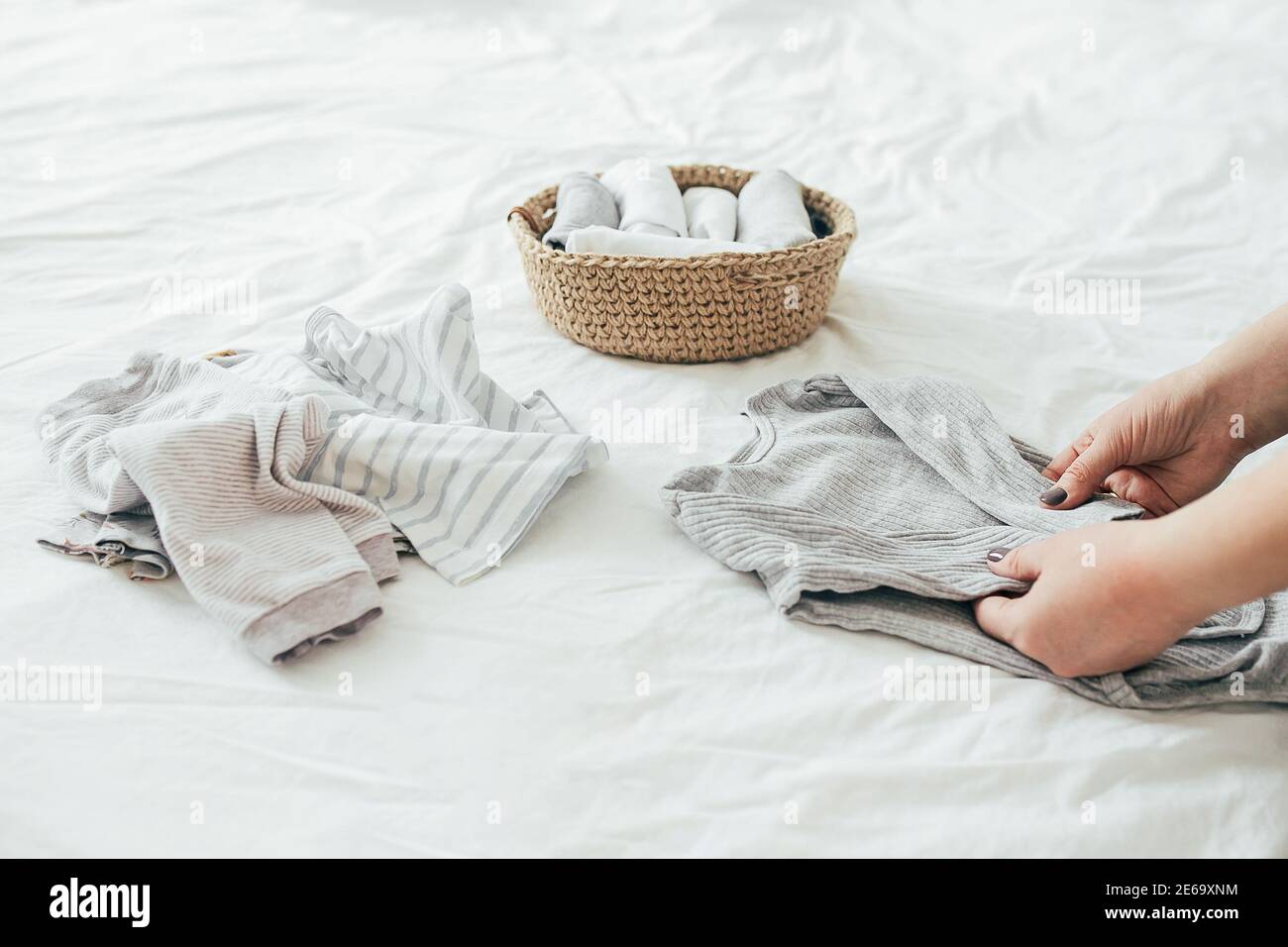 Donna che piega i vestiti in cesto di iuta nel sistema di konmari. Concetto di organizzazione di abiti minimalisti. Foto Stock