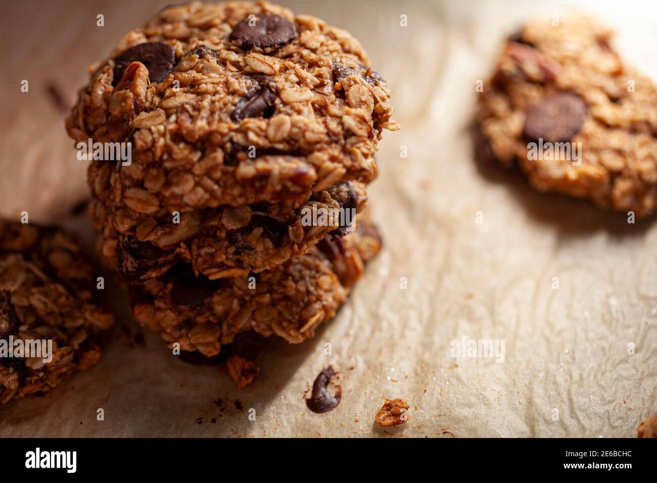 Accatastati biscotti appena fatti su carta da forno. Questi sono fatti con avena intera di grano arrotolata con i trucioli di cioccolato scuro. Ci sono pezzi e crumbles sopra Foto Stock