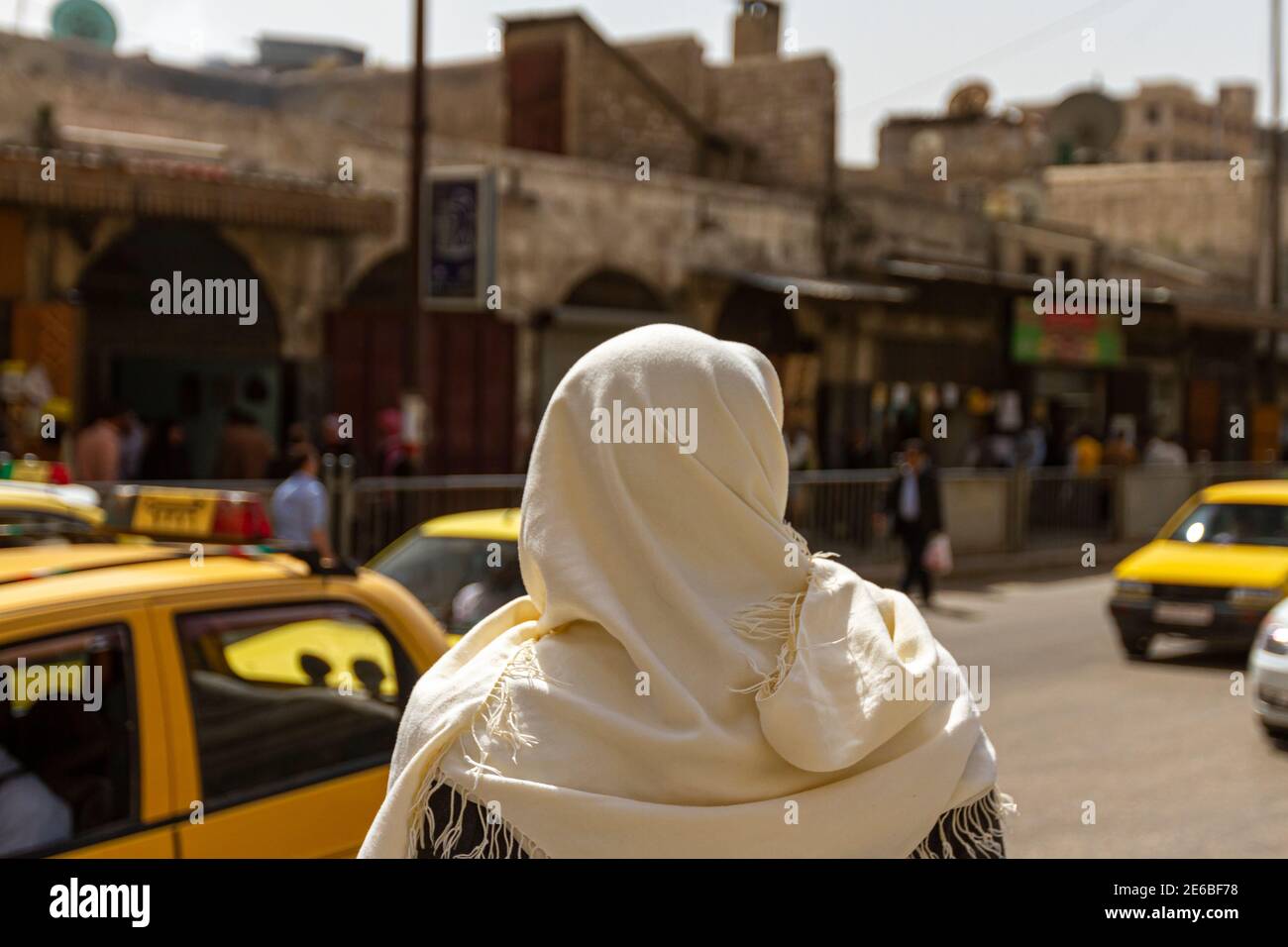 Un siriano che indossa abiti tradizionali locali è in piedi su una strada trafficata nel quartiere storico della città siriana settentrionale di Aleppo. Retro sfocato Foto Stock