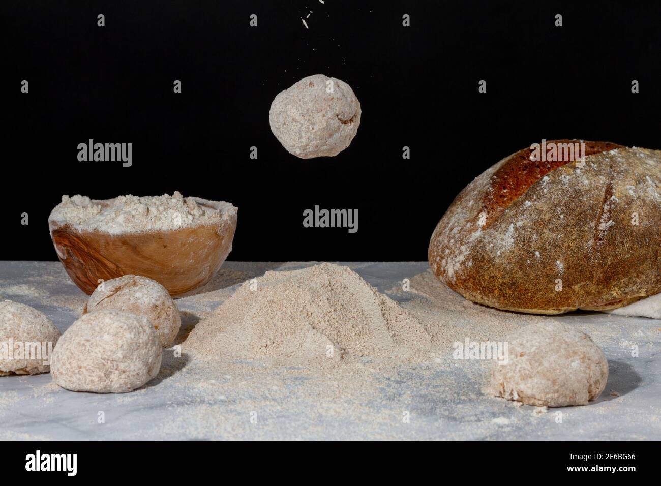 Un impasto di pane arrotondato sta cadendo su un mucchio di farina sul piano di marmo. A terra ci sono pani e impasti, una ciotola di farina e un RU Foto Stock