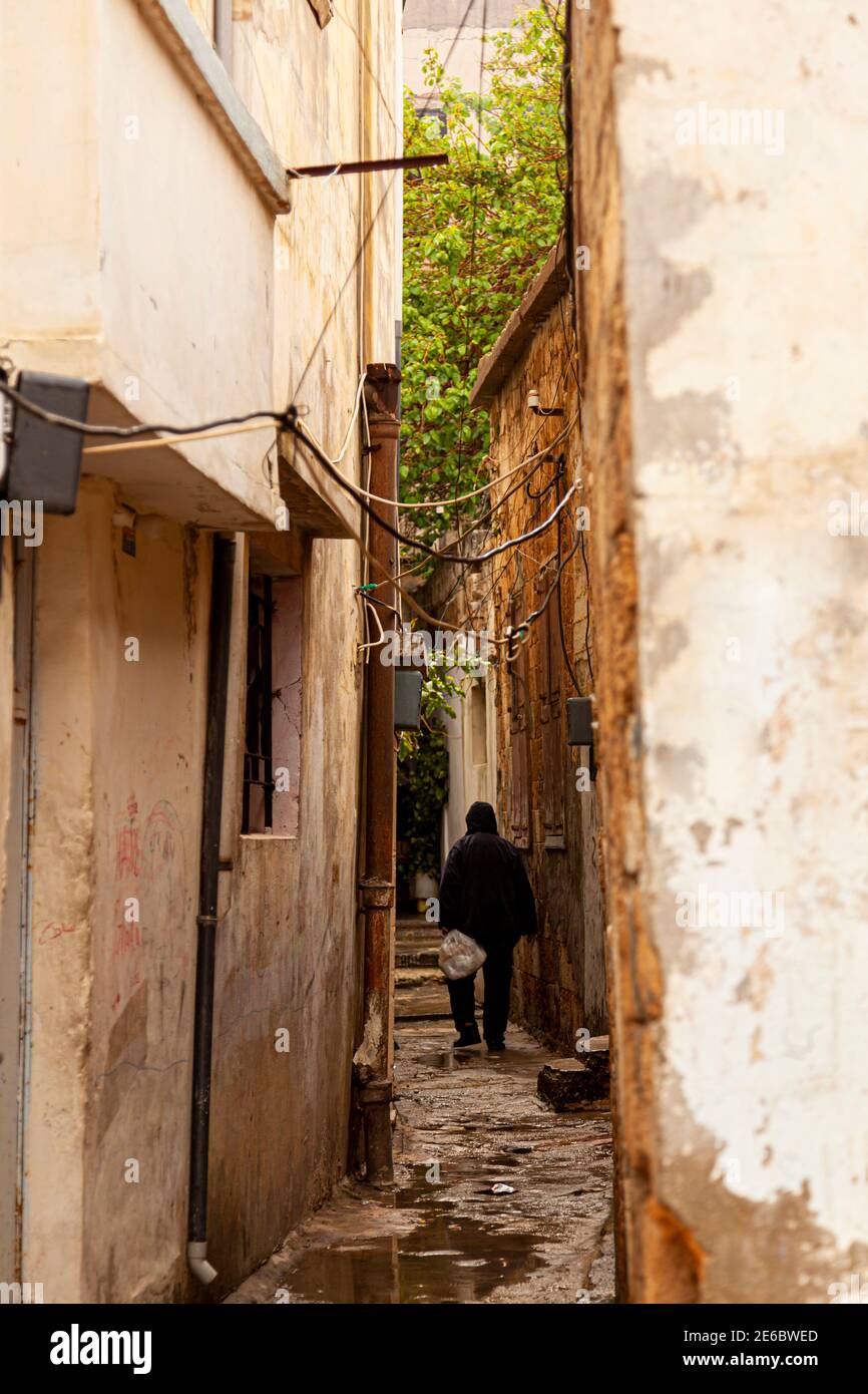 Un vicolo stretto in un quartiere a basso reddito della città vecchia a Damasco, Siria. Le case sono scappate con i cavi dei trucioli di vernice appesi tra gli edifici. Pioggia p Foto Stock