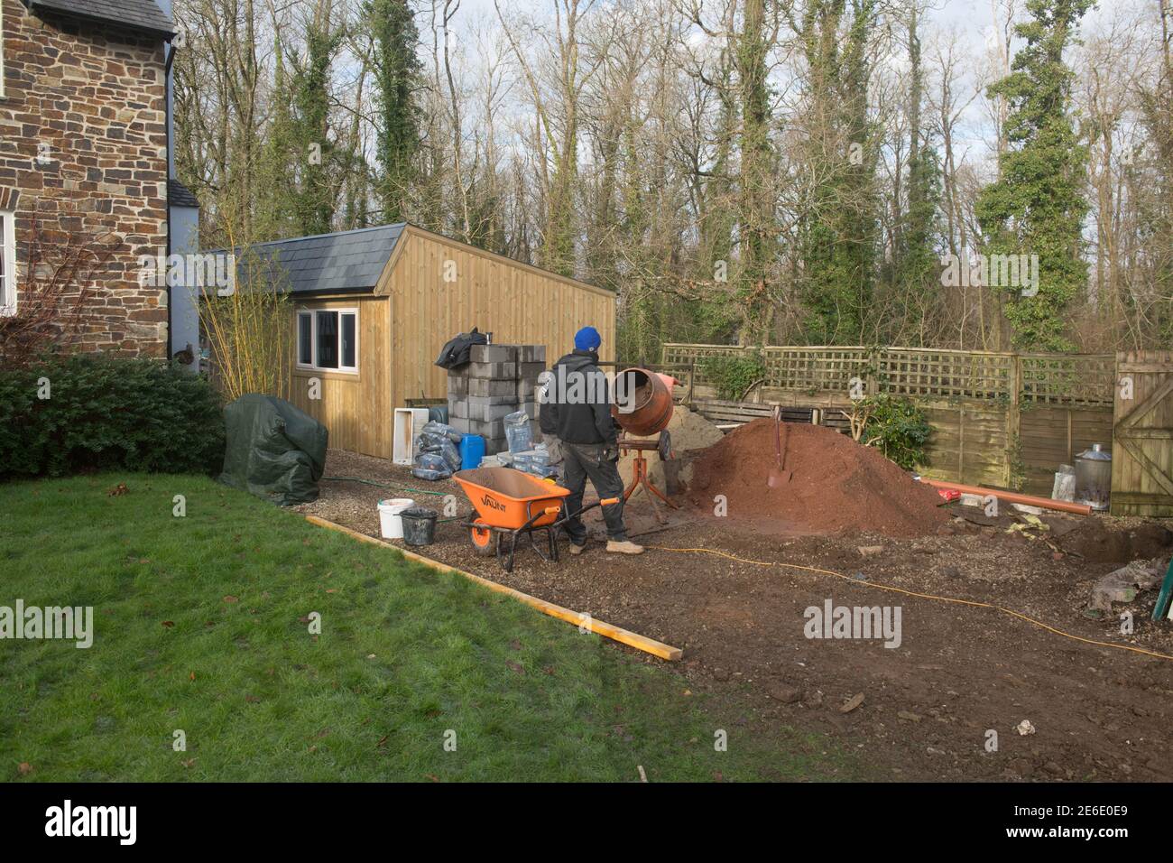 Operai o costruttori che mescolano calcestruzzo su un luogo di costruzione in un giardino rurale in Devon rurale, Inghilterra, Regno Unito Foto Stock
