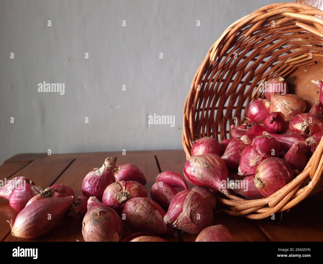 Scalogni in un cesto di vimini che si inclina e si riversa sono sparsi su un tavolo di legno Foto Stock