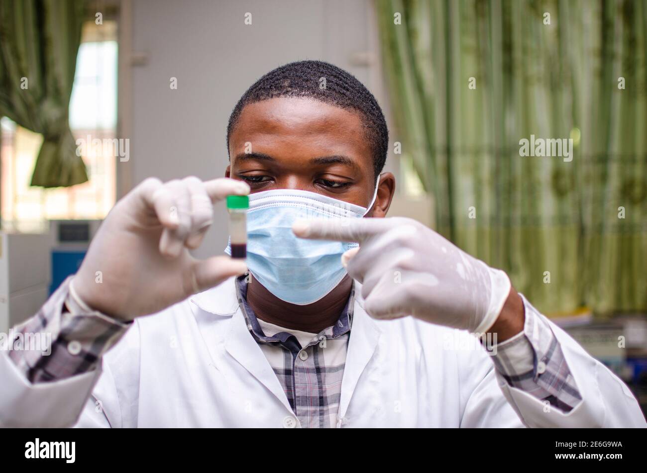 Giovane scienziato di laboratorio nero che indossa una maschera al naso, osservando un campione di sangue in mano Foto Stock